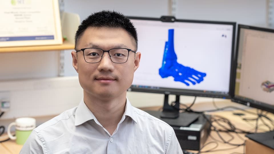 Hengshuo in a engineering lab with a graphic of a blue coloured foot on his computer